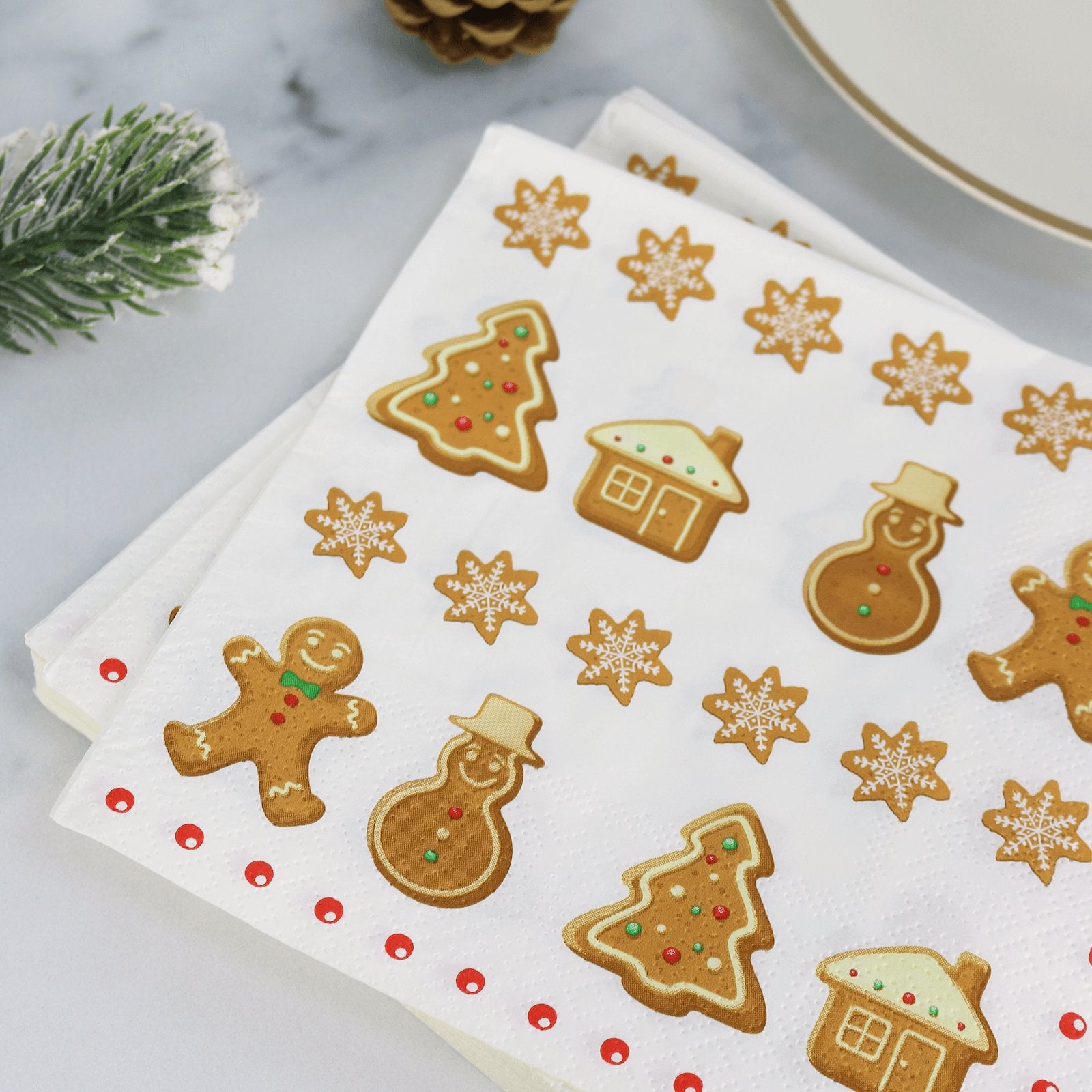 gingerbread paper table napkins on table beside gold trim plate and pine cones